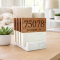 Wooden and marble coasters displaying "75078 prosper, tx" stand neatly on a wooden table. A potted succulent and cozy living room decor are in the background.
